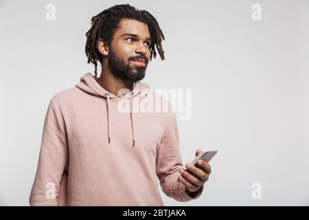 Porträt eines jungen afrikanischen Mannes mit Hoodie, der isoliert auf weißem Hintergrund steht und das Mobiltelefon benutzt Stockfoto