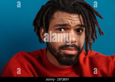 Portrait Nahaufnahme von unglücklichen afroamerikanischen Mann posiert und Blick auf Kamera isoliert über blauem Hintergrund Stockfoto