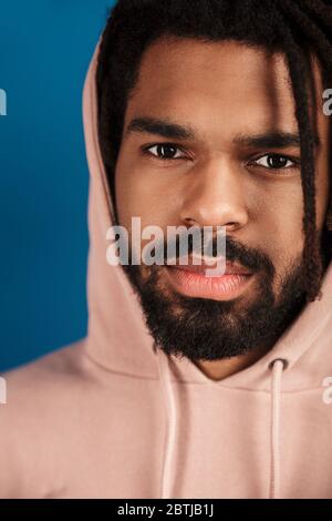 Porträt des bärtigen afroamerikanischen Mann in der Kapuze posiert und Blick auf Kamera isoliert über blauem Hintergrund Stockfoto