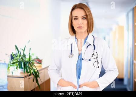 Porträtaufnahme einer selbstbewussten Ärztin, die im Krankenhausskorridor auf die Kamera schaut. Stockfoto
