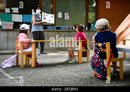 Ivrea, Italien - 26. Mai 2020: Ein Lehrer liest ein Buch zu den Kindergartenkindern in einem Schulgarten. Die Gemeinde Ivrea eröffnet die Gärten zweier Kindergartenschulen im Rahmen eines Pilottests, um zu sehen, wie die Schulen nach der Sperrung des Coronavirus COVID-19 wieder eröffnet werden können. Quelle: Nicolò Campo/Alamy Live News Stockfoto