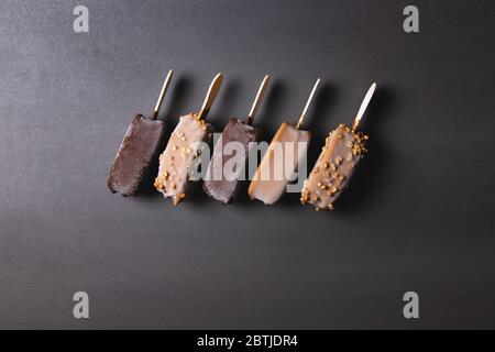 Verschiedene Schokoladeneis-Eis-Eiszapfen, auf schwarzem Hintergrund ausgekleidet. Dunkle Schokolade, mit Nüssen und Milchschokolade-Eis Stockfoto
