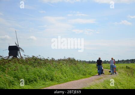 Eltern mit ihren Kindern für einen Spaziergang an heißen Sommertagen. Sonniger Tag in Kinderdijk mit Windmühlen. Stockfoto