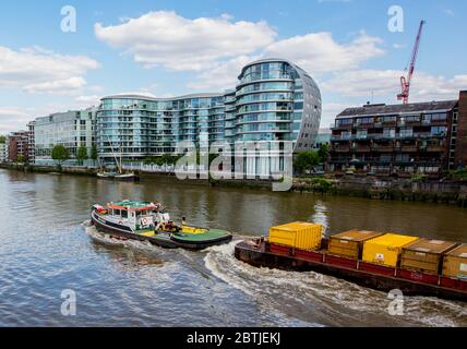 Die Albion Riverside Entwicklung, Battersea, London, zeigt Wohn- und Geschäftseinheiten; entlang der Themse ein Lastkahn zieht Container. Stockfoto