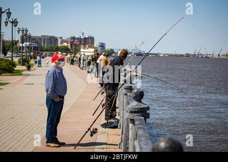 Astrachan/Russland - 25. Mai 2020: Ein älterer Mann in einer medizinischen Maske fängt Fische an der Uferpromenade der Stadt Astrachan Stockfoto