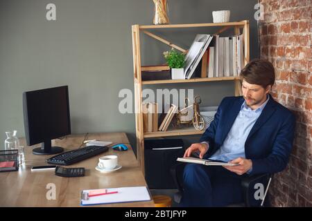 Überprüfen von Dokumenten, Aufgaben und Unterlagen. Der junge Mann, Manager, kehrt nach der Quarantäne in sein Büro zurück, fühlt sich glücklich und inspiriert. Rückkehr zum normalen Leben. Business, Finanzen, Emotionen Konzept. Stockfoto