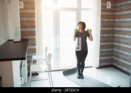 Erwachsene fit schlanke Frau hat Training zu Hause. Ältere weibliche Person stehen mit Hanteln auf und bereit zu trainieren. Allein im Zimmer. Slim Fit Frau kümmern Stockfoto