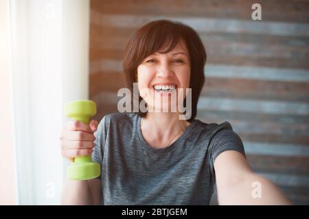 Erwachsene fit schlanke Frau hat Training zu Hause. Fröhlich positiv glücklich Erwachsene ältere weibliche Person Lächeln. Gut gebaute wunderschöne Frau halten eine grüne Hantel Stockfoto