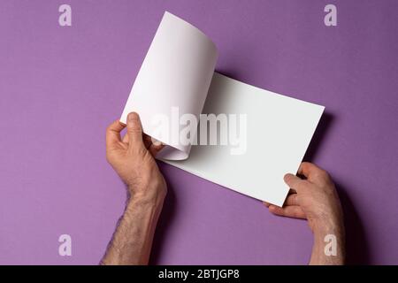 Männliche Hand öffnete einen Katalog auf lila Hintergrund, Mock-up-Serie Vorlage bereit für Ihre Design-Auswahl-Pfad enthalten Stockfoto