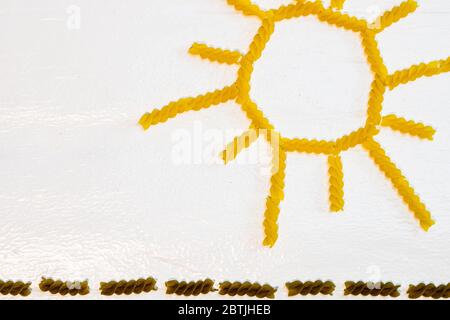 Sonne aus Fusilli Pasta, grünes Feld aus grüner Spirale Pasta auf weißem Hintergrund Stockfoto