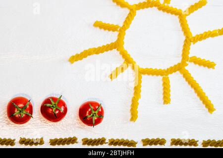 Sonne aus Fusilli Pasta, grünes Feld aus grünen Spiral-Pasta und Kirschtomaten, Konzept des Anbaus von Tomaten auf weißem Hintergrund Stockfoto