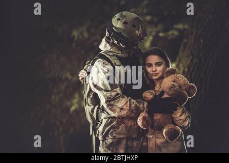 Kaukasischer Soldat in den 30er Jahren im Tarnanzug Rückkehr von der Armeemission und Treffen mit seiner Tochter. Familie Wiedervereint. Mädchen mit Teddybär in den Händen sie Stockfoto