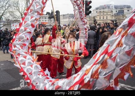 Lady in rotem Kostüm winken Teil einer Drachen-Requisite. Konzentriere dich auf die Dame. Parade Zur Chinesischen Neujahrsfeier. London Stockfoto