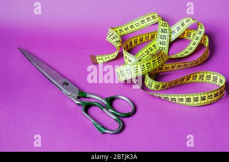 Alte Metallschere und ein gelbes Maßband auf violettem Hintergrund. Schneiderwerkzeuge. Handarbeit und Handwerk. Nahaufnahme. Kopierbereich. Stockfoto