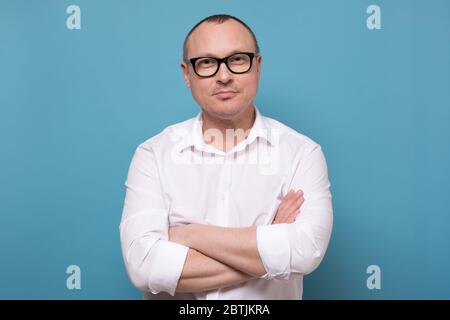 Lächelnder reifer Mann in Brille und weißem Hemd stehend mit Gefaltete Hände Stockfoto
