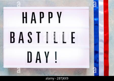 Happy Bastille Day in Leuchtkasten auf blauem Himmel Hintergrund geschrieben. 14. Juli Konzept für Grußkarte, Festplakat etc Stockfoto