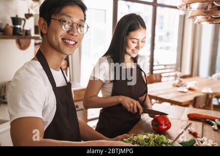 Bild von jungen multikulturellen Paar in Schürzen lachen und Mittagessen in der gemütlichen Küche Stockfoto