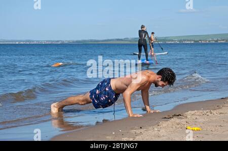 Portobello, Edinburgh, Schottland, Großbritannien. 26 Mai 2020. Entspanntere Atmosphäre am Meer am späten Nachmittag, als Schottland sich dem Ende der Phase 1 der Coronavirus Lockdown nähert. Temperatur von 19 Grad und sonnig. Abgebildet die Familie Harrison, genießen Mama und einer ihrer Söhne Stand-up Paddle Boarding, während der andere Sohn Übungen mit Druck auf am Ufer des Sandstrandes. Quelle: Arch White/Alamy Live News. Stockfoto