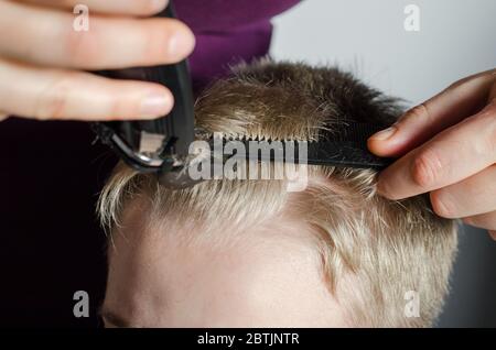 Frau schneidet zu Hause die Haare des Jungen. Haushaarschnitt durch Haarschneider. Stockfoto
