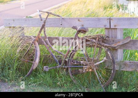 Ein altes verlassene rostige Fahrrad parkte gegen Holzzaun. Altmodische klassische Fahrrad steht vergessen entlang eines Radweges. Aus dem Graben gefischt Stockfoto