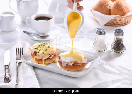 Frühstück.Beste Eier Benedict - gebratene englische Brötchen, Schinken, pochierte Eier, Bewässerung Hollandaise Butter Sauce aus der Soße Boot Stockfoto