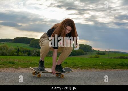 Ein junges Mädchen hockt Skateboarding auf einer Straße in grüner Natur Stockfoto