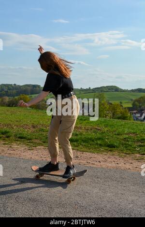 Girl reitet ein Skateboard auf einer Landstraße in grüner Natur Stockfoto