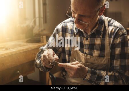 Reifer Zimmermann arbeitet mit seinen Händen an einem Geigenbogen Stockfoto