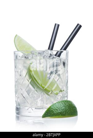 Gimlet-Cocktail in Kristallglas mit Eiswürfeln und Stroh und Limettenscheiben auf weißem Hintergrund mit Limette an der Seite. Stockfoto