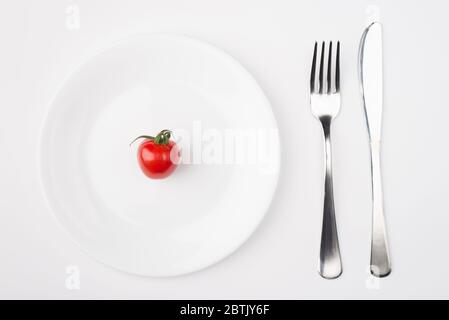 Essen auf einem kalorienarmen Konzept. Oben oben oben oben Ansicht Foto von einem Teller mit einer einzigen Tomate mit Gabel und Messer auf der rechten Seite platziert isoliert o Stockfoto
