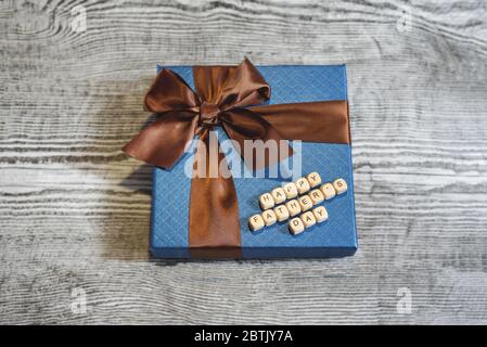 Ein blaues Geschenk mit braunem Streifen auf dem Holzhintergrund. Ein Schild Happy Father's Day aus Holzblöcken. Konzept des Vatertags. Stockfoto