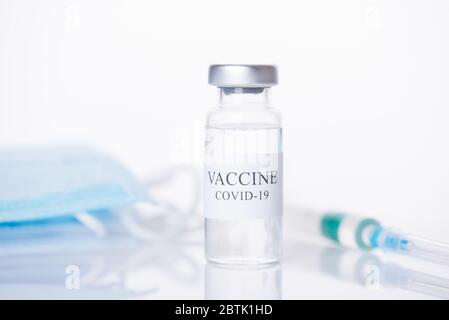 Infektionskrankheiten Medizin Medicare Konzept. Nahaufnahme von COVID-19 Impfstoff Fläschchen mit verschwommenem Schuss und Masken hinter isoliert auf weißem Hintergrund Stockfoto