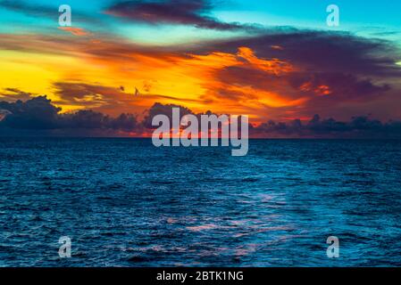 Foto eines spektakulären feurigen orangefarbenen Sonnenuntergangs über dem tiefblauen Wasser des Indischen Ozeans Stockfoto