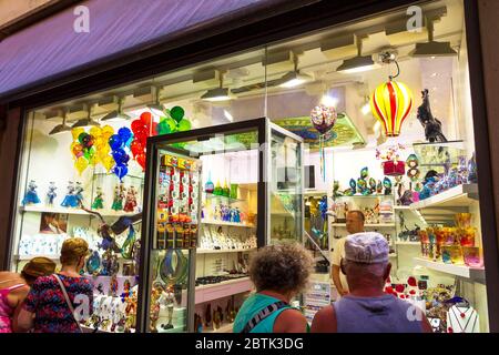 Touristen, die ein Schaufenster mit Murano-Glas in einer Geschäftsstraße nahe dem Markusplatz in der Altstadt von Venedig, Italien, im Juni 2016, sehen Stockfoto