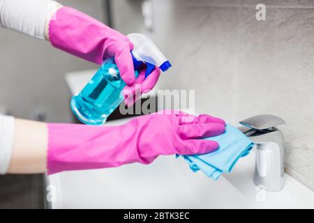 Weibliche Hände tragen Gummihandschuhe halten Mikrofasertuch und Sprühflasche Desinfektionsmittel zu desinfizieren Waschbecken Wasserhahn im Bad. Schutz vor Viren Stockfoto