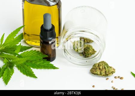 Glasflaschen mit ätherischem CBD-Öl, medizinischen Marihuana-Blättern, Knospen und Samen auf weißem Hintergrund, Nahaufnahme. Konzepte der alternativen oder pflanzlichen medici Stockfoto