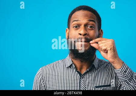 Ich werde kein Wort sagen. Schwarzer bärtiger Kerl, der mit der Hand die Lippen überspringt und zeigt, dass er ein geheimes, blaues Studio halten wird Stockfoto