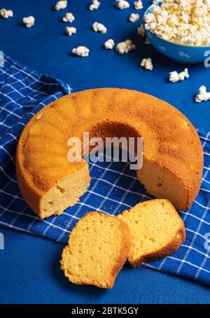 In Scheiben geschnittener Maismehlkuchen und eine Schale Popcorn auf einem blauen Tisch. Traditionelle brasilianische Süßspeisen mit Maismehl. Festa Junina Essen Stockfoto