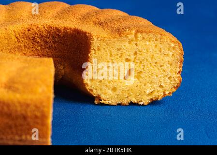 Nahaufnahme eines in Scheiben geschnittenen Maismehltörchens auf blauem Hintergrund. Biskuitkuchen mit Maismehl. Fest Junina traditionelle Dessert Stockfoto