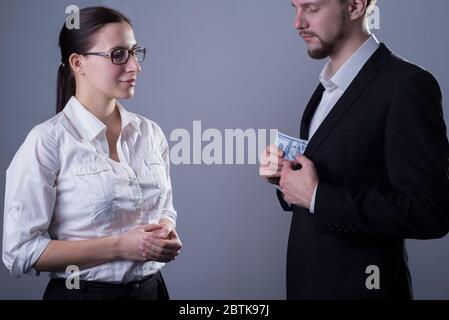 Porträt von zwei jungen Geschäftsleuten in Business-Kleidung. Eine Geschäftsfrau mit Brille beobachten einen Mann, nehmen eine Presse von Dollar-Rechnungen aus seiner Jacke p Stockfoto