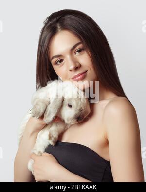 Porträt eines jungen fröhlichen Mädchens mit einem weißen Tierkaninchen in den Armen. Auf grauem Hintergrund Stockfoto
