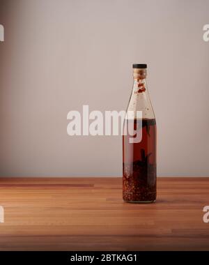 Transparente Flasche hausgemachtes Chilliöl mit Stücken von trockenem Chili, auf einem Holztisch Stockfoto