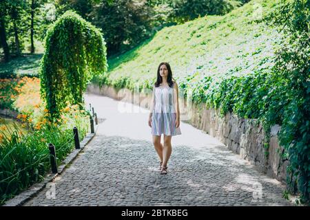 Sofia Park, Uman. Das Mädchen geht an einem sonnigen Tag durch die Gassen des Parks. Brunette Mädchen in einem weißen Kleid Spaziergänge in einem schönen Landschaftspark. Pfad Stockfoto