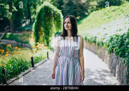 Sofia Park, Uman. Das Mädchen geht an einem sonnigen Tag durch die Gassen des Parks. Brunette Mädchen in einem weißen Kleid Spaziergänge in einem schönen Landschaftspark. Pfad Stockfoto