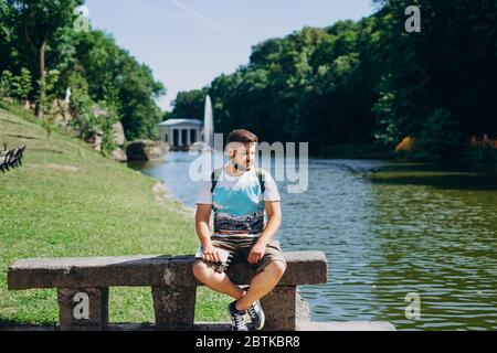 Sofia Park, Uman. Schöner junger Mann sitzt auf einer Bank auf dem Hintergrund des Sees. Männlicher Tourist mit Rucksack auf einer Bank auf der Rückseite sitzend Stockfoto