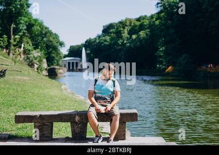 Sofia Park, Uman. Schöner junger Mann sitzt auf einer Bank auf dem Hintergrund des Sees. Männlicher Tourist mit Rucksack auf einer Bank auf der Rückseite sitzend Stockfoto