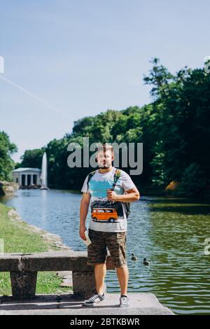 Sofia Park, Uman. Schöner Mann mit Rucksack und T-Shirt auf dem Hintergrund eines schönen Sees. Junger Mann auf dem Hintergrund des Sees mit einem Tal Stockfoto