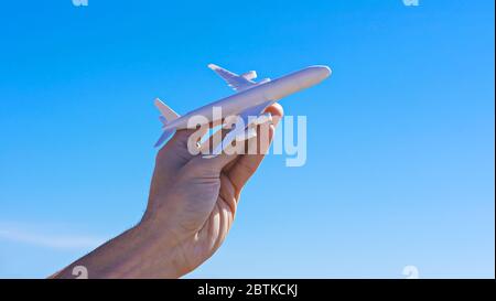 Flugzeugmodell in der Hand gegen klaren blauen Himmel. Das Flugverbot wird ausgesetzt. Konzept der COVID-19-Pandemie iv-Überschuß des Coronavirus. Länder öffnen Grenzen, offene Flüge, Reiseboom Stockfoto