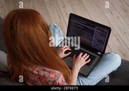 Junge rothaarige kaukasische Frau Programmierer Arbeiter mit Laptop arbeiten von zu Hause, Freiberufler, soziale Distanz und Remote-Arbeit Stockfoto