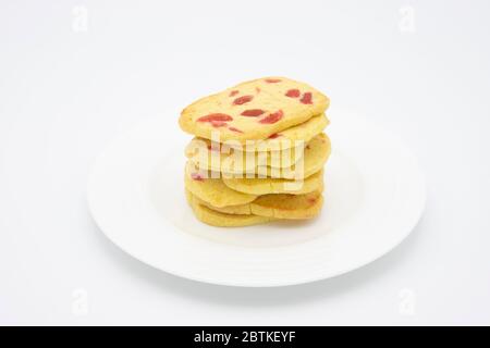 Ein Haufen traditioneller, knuspriger Scheiben und gebackener Plätzchen, hausgemachte goldene Kekse mit Stücken roter Kirsche auf einem weißen Teller Stockfoto